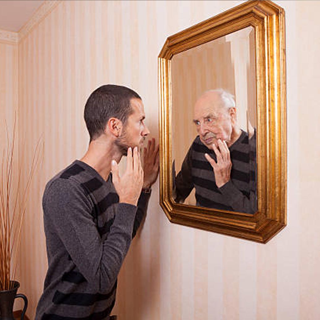 40 is the new 80? Young man looking into the mirror at an old reflection of himself